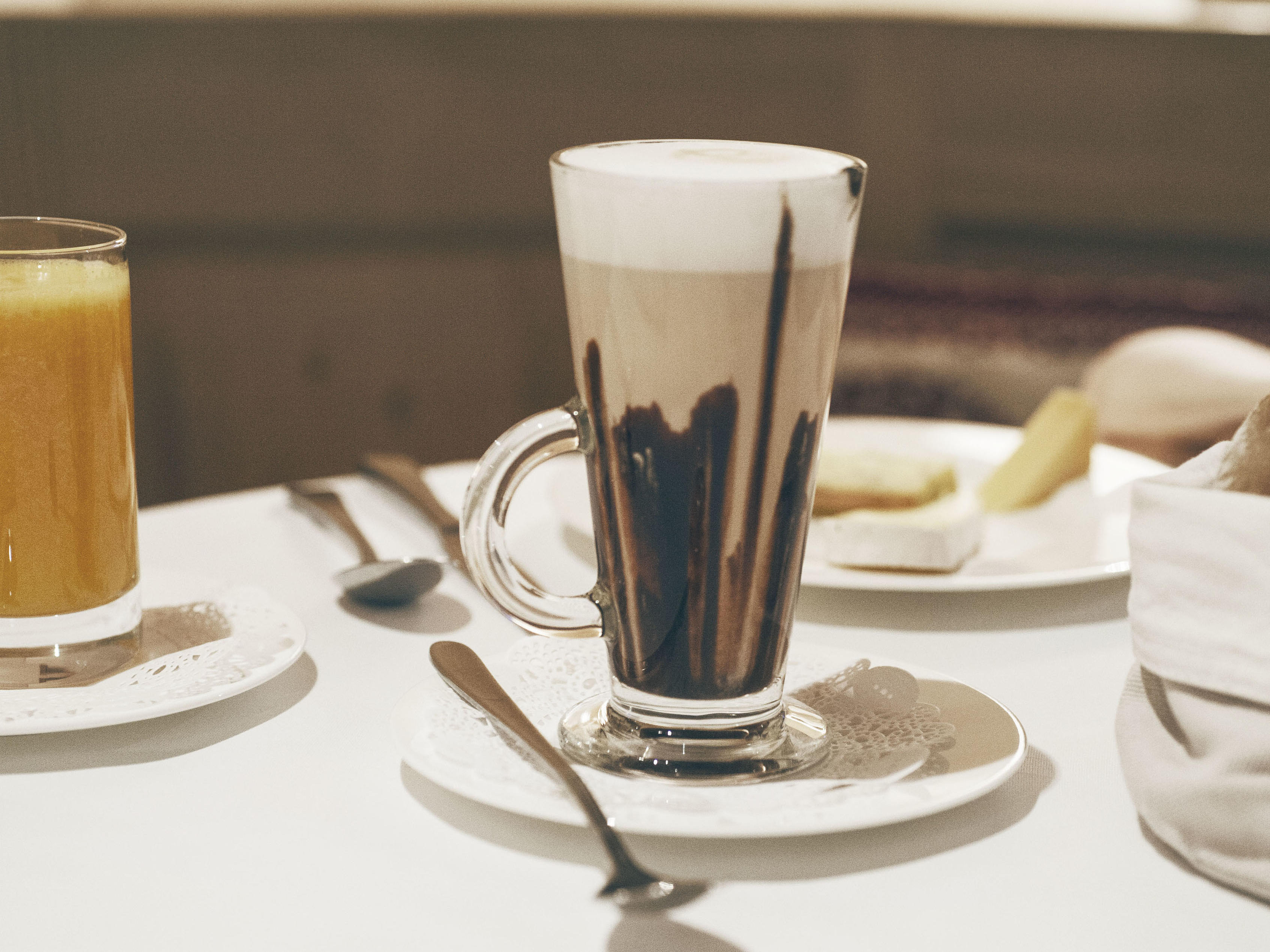 Latte Macchiato mit Schokosirup Hohes Glas Latte Macchiato mit Schokosirup auf weißem Tisch